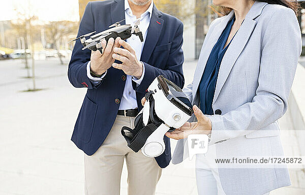 Eine Ingenieurin hält ein Virtual-Reality-Headset neben einem männlichen Kollegen mit einer Drohne im Büropark