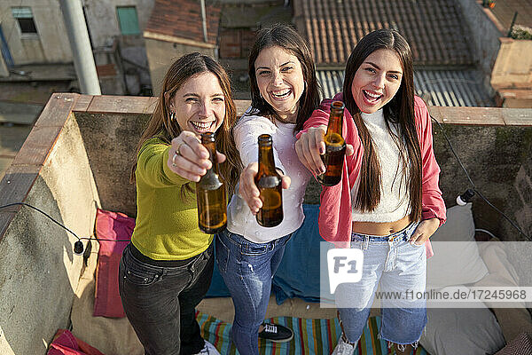 Fröhliche Freundinnen heben eine Bierflasche  während sie sich auf dem Dach vergnügen