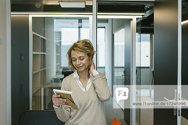 Lächelnde Unternehmerin mit Hand im Haar  die einen Fotorahmen im Büro betrachtet