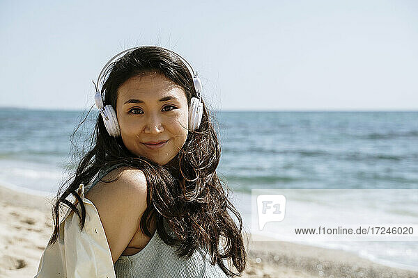 Schöne Frau mit Kopfhörern lächelnd am Strand an einem sonnigen Tag