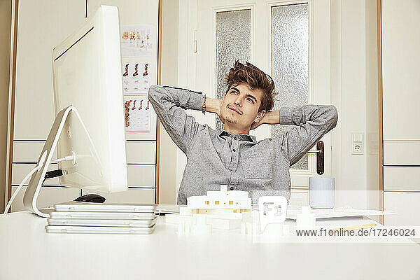 Junger männlicher Architekt mit Händen hinter dem Kopf träumt  während er im Büro sitzt