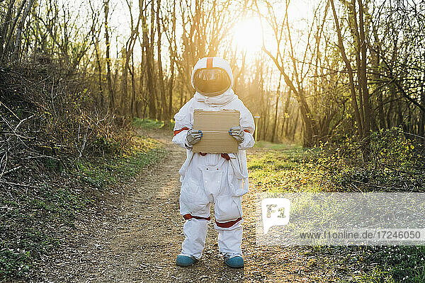 Junge Astronautin im Raumanzug hält Karton auf Waldweg