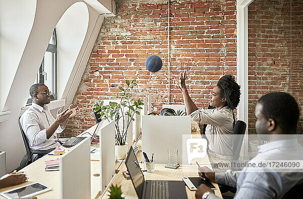 Männliche und weibliche Unternehmer spielen mit einem Ball im Coworking-Büro