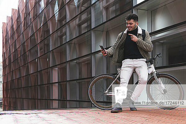 Smiling businessman pointing during video call while leaning on bicycle