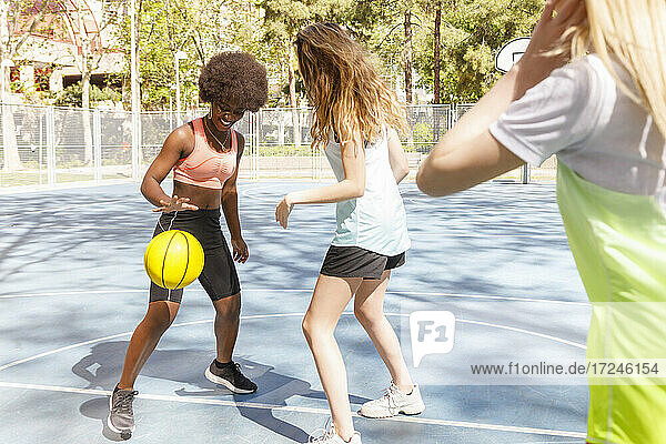 Female friends playing basketball in sports court at park