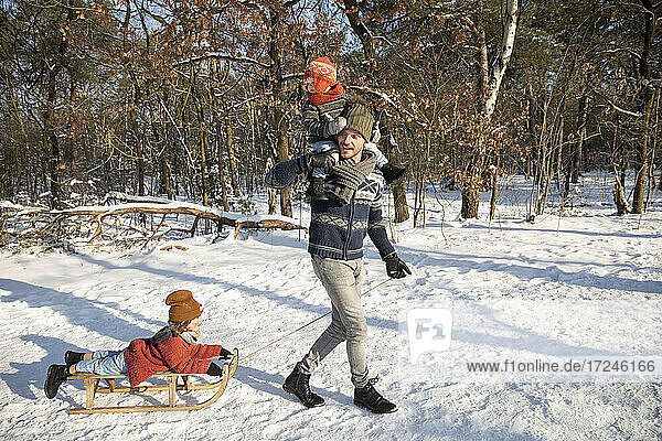 Vater trägt seinen Sohn auf der Schulter  während er im Winter einen Schlitten durch den Schnee zieht