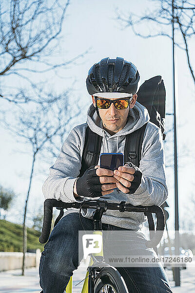 Älterer Zusteller  der sich auf ein Fahrrad stützt und ein Smartphone benutzt