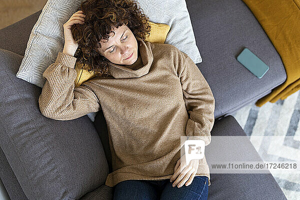 Frau entspannt sich mit Handy auf Sofa im Wohnzimmer zu Hause