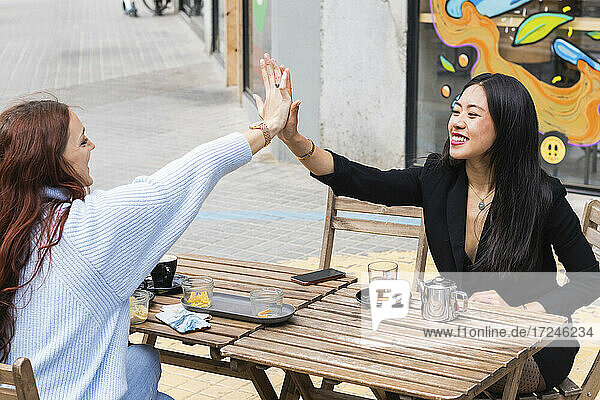 Lächelnde Freundinnen  die sich beim Sitzen in einem Straßencafé die Hände reichen