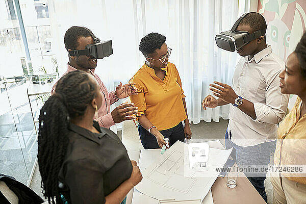 Male design professionals watching virtual reality through headsets by female colleagues in coworking office