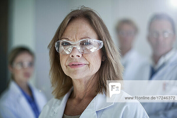 Female doctor wearing protective glasses with colleagues in background at hospital