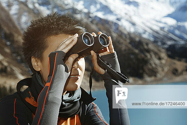 Mid adult woman looking through binoculars by lake during vacations