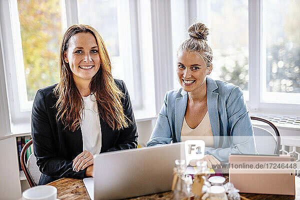Happy female entrepreneurs sitting with laptop in office