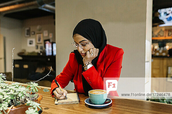 Junge Geschäftsfrau schreibt in einem Café in ihr Tagebuch