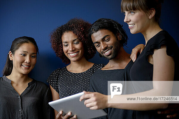 Lächelnde internationale männliche und weibliche Fachkräfte arbeiten an einem digitalen Tablet vor einem blauen Hintergrund