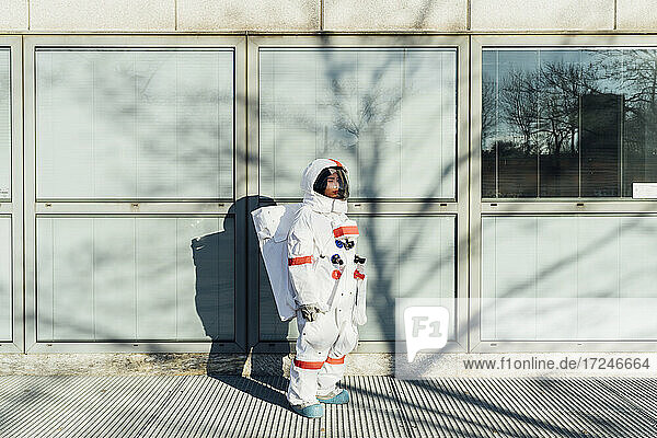 Junge Astronautin im Raumanzug steht an einem Glasfenster in der Stadt an einem sonnigen Tag