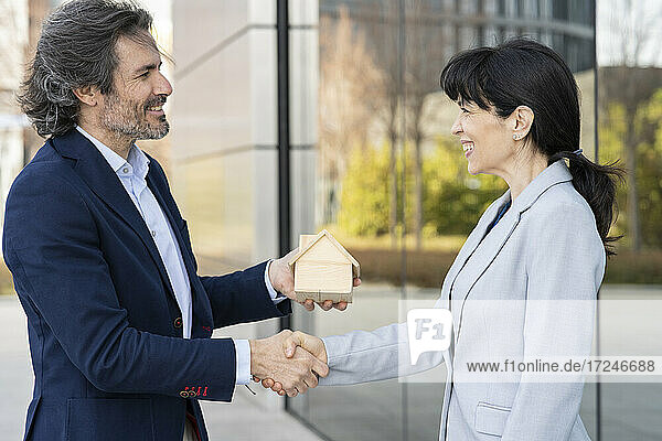 Lächelnde Geschäftsfrau beim Händeschütteln mit einem Immobilienentwickler  der ein Hausmodell hält