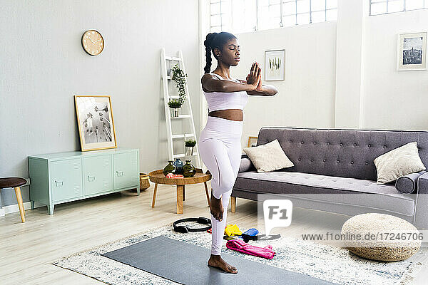 Junge Frau  die auf einem Bein steht  während sie zu Hause Yoga macht