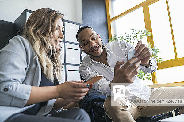 Lächelnder männlicher Fachmann  der einer weiblichen Kollegin in einem Coworking-Büro sein Mobiltelefon zeigt