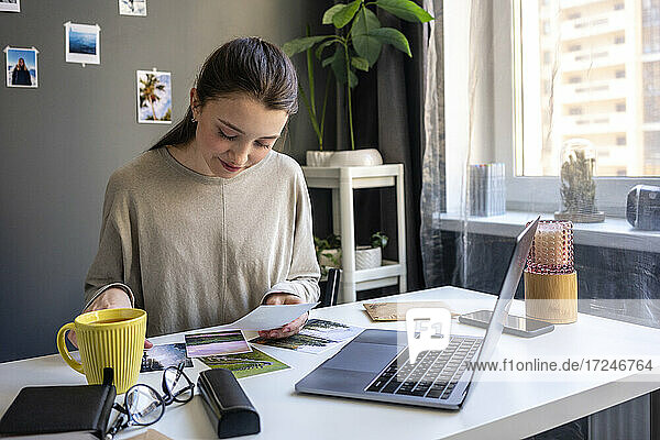 Junge Frau überprüft ein Foto  während sie zu Hause am Laptop sitzt