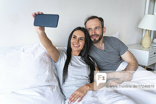 Frau nimmt Selfie mit Mann durch Smartphone auf Bett zu Hause