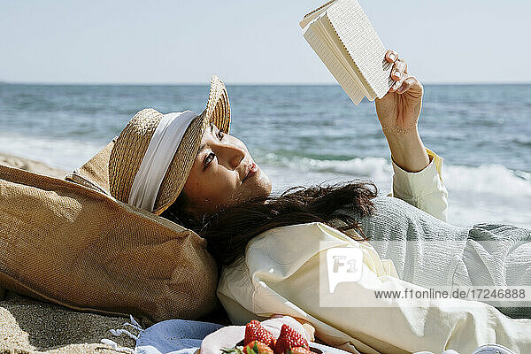 Frau liest ein Buch  während sie am Wochenende am Strand liegt
