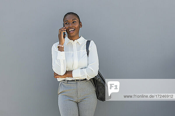 Female entrepreneur talking on mobile phone while standing in front of gray wall