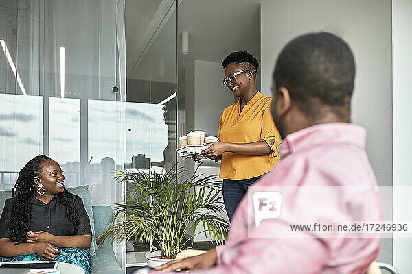 Lächelnde Geschäftsfrau  die männlichen und weiblichen Mitarbeitern im Büro Kaffee anbietet
