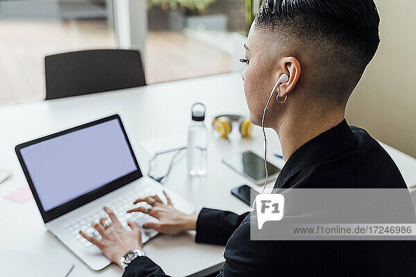 Junge Geschäftsfrau mit In-Ear-Kopfhörern bei der Arbeit am Laptop im Büro