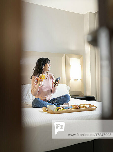 Lächelnde Frau schaut weg  während sie in einer Hotelsuite einen Saft trinkt