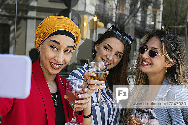Junge Frau macht Selfie mit Freundinnen bei einem Drink