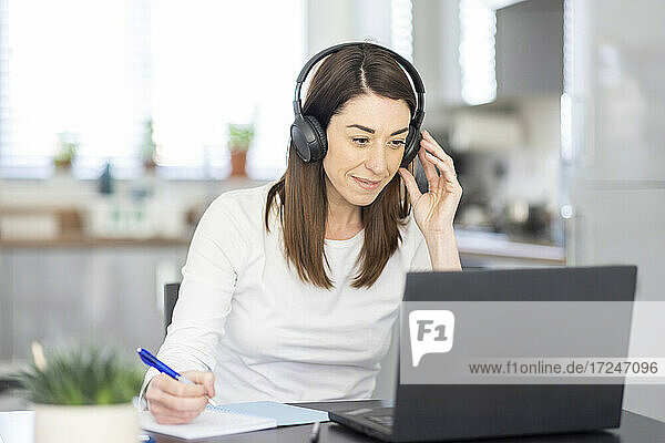 Smiling female entrepreneur wearing headphones working at home