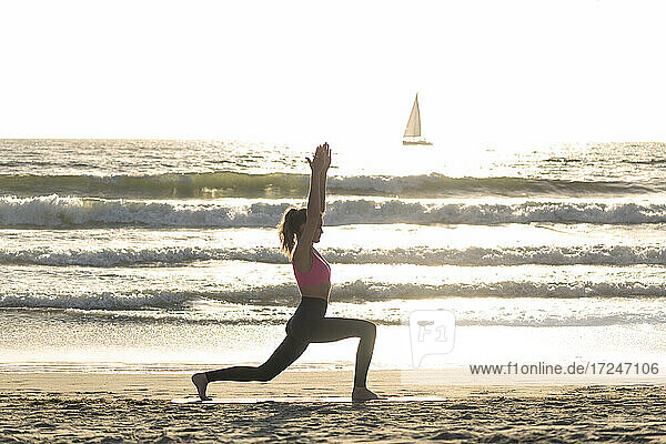 Frau übt Yoga am Meeresufer an einem sonnigen Tag