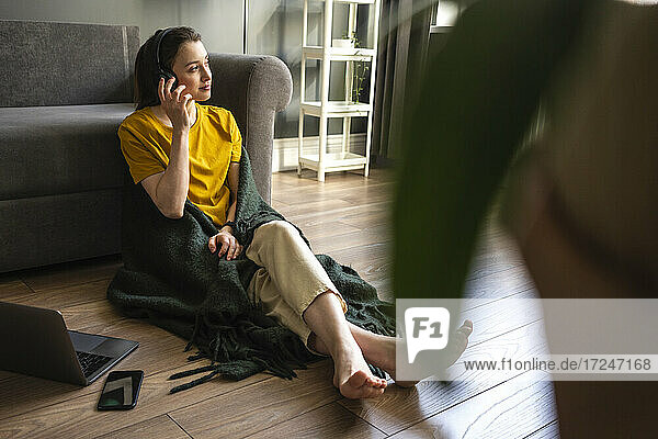 Woman listening music through headphones while sitting by laptop and mobile phone at home
