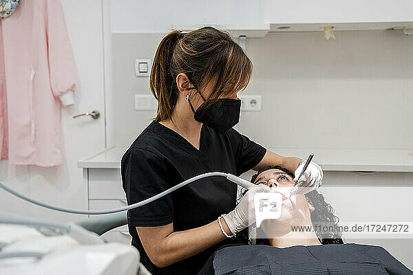Zahnärztin mit Gesichtsschutzmaske beim Absaugen eines Patienten in der Klinik