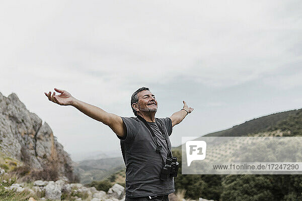 Carefree man standing with arms outstretched on mountain