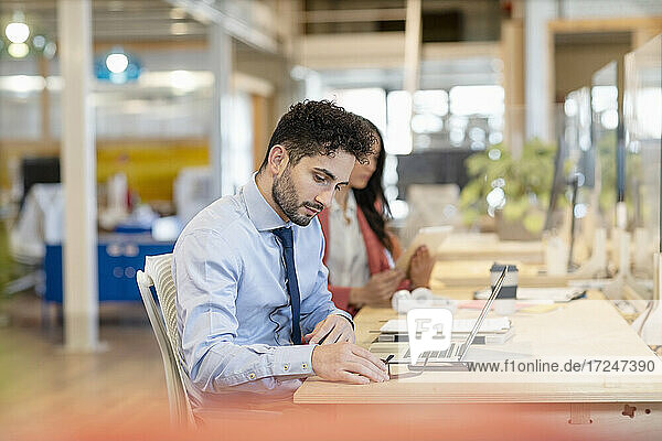 Young businessman working by female colleague in office