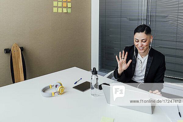 Lächelnder Profi winkt mit der Hand während eines Videoanrufs über einen Laptop im Büro