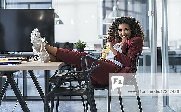 Glückliche weibliche Fachkraft mit hochgelegten Füßen  die sich auf einem Stuhl in einem Coworking-Büro entspannt