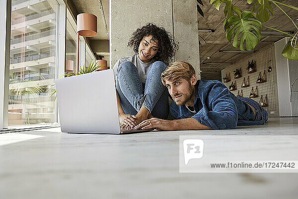 Mann benutzt Laptop mit Freundin auf dem Boden seiner Wohnung