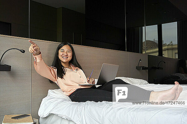 Lächelnde weibliche Fachkraft  die mit einem Laptop im Hotel sitzt und darauf zeigt