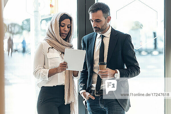 Businesswoman discussing with businessman over digital tablet at entrance of office