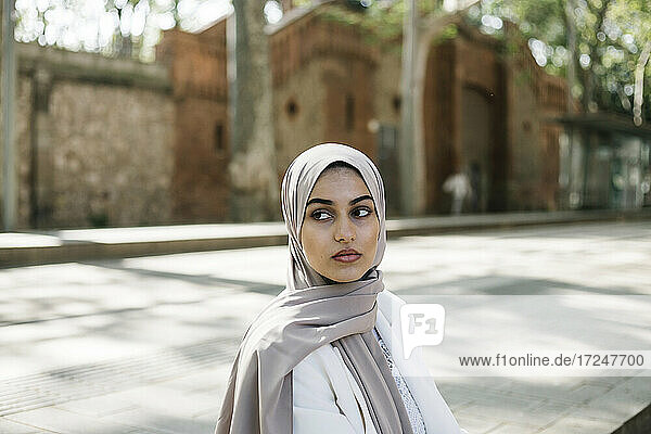 Junge Frau mit Hidschab  die auf dem Gehweg sitzt und wegschaut