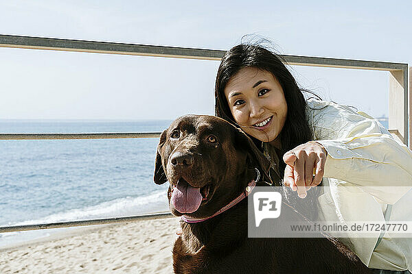 Schöne Frau mit Labrador-Hund  der auf einen sonnigen Tag am Strand zeigt