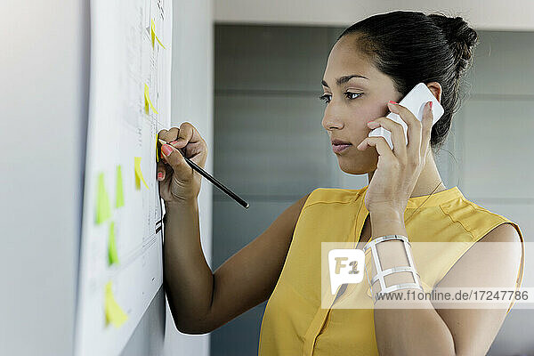Junge Geschäftsfrau  die bei der Arbeit im Büro mit ihrem Mobiltelefon telefoniert