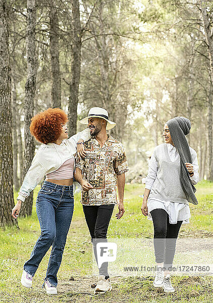 Happy female friends with young man having fun during picnic in forest