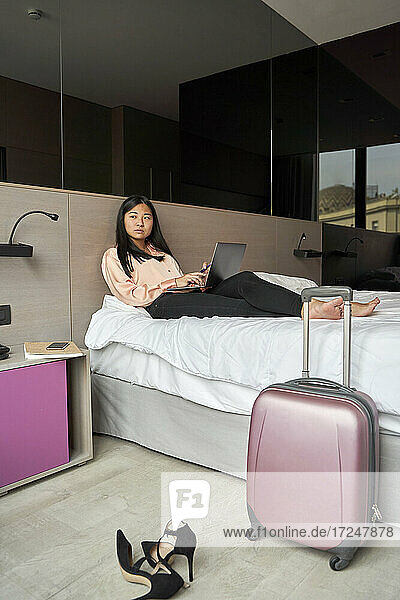 Nachdenkliche Geschäftsfrau  die wegschaut  während sie mit ihrem Laptop auf dem Bett im Hotel sitzt