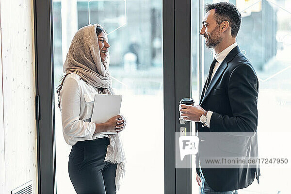Lächelnde männliche und weibliche Geschäftsleute stehen von Angesicht zu Angesicht am Eingang eines Büros