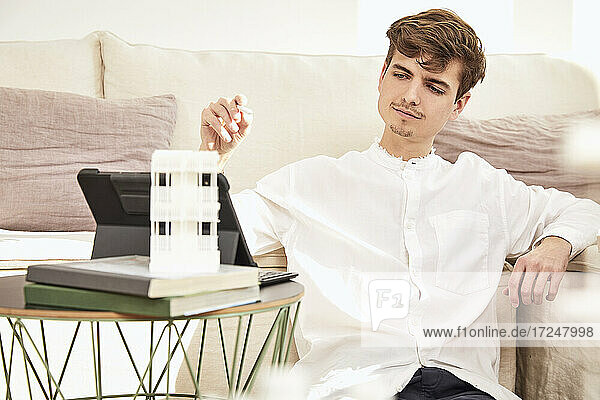 Male architect observing architectural model while sitting at home