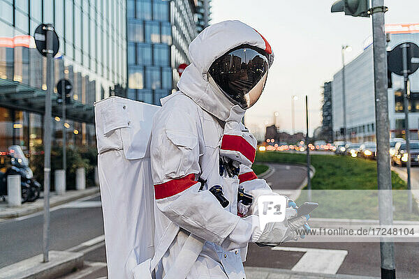 Männlicher Astronaut im Raumanzug  der auf einer Straße in der Stadt ein Mobiltelefon benutzt